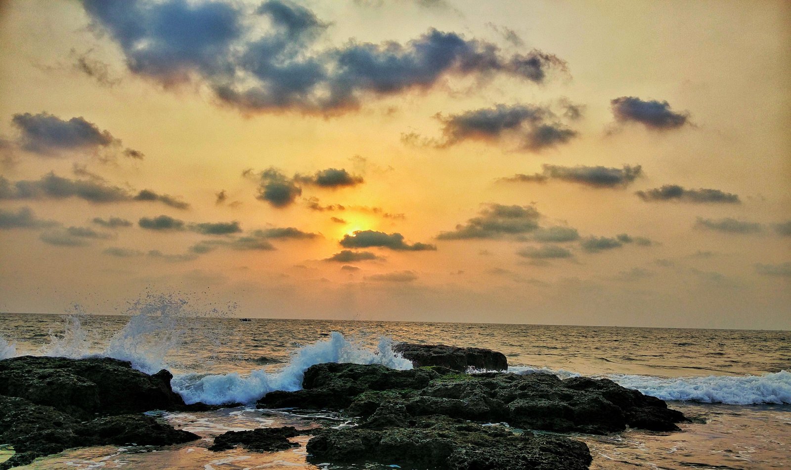 Golden sunset and waves breaking over the dark rocks at Anjuna Beach, Goa